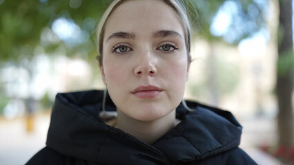 Young blonde woman standing with serious expression at park