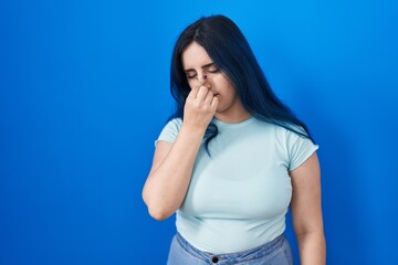 Young modern girl with blue hair standing over blue background tired rubbing nose and eyes feeling fatigue and headache. stress and frustration concept.