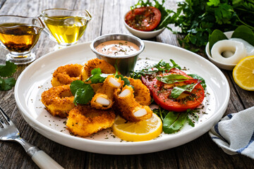 Fried breaded calamari rings with lemon and fresh vegetables on wooden table
