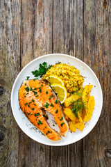 Fried salmon steak with French fries and fresh vegetable salad served on wooden table
