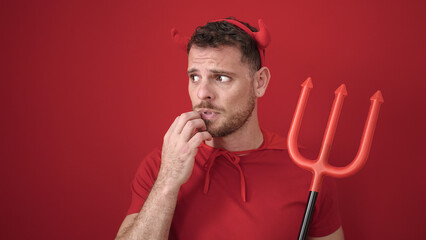Young caucasian man looking afraid wearing devil costume over isolated red background