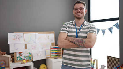 Young caucasian man working as teacher smiling with crossed arms at kindergarten