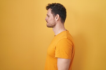 Young hispanic man standing over yellow background looking to side, relax profile pose with natural face and confident smile.