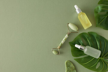Natural cosmetic products concept. Flat lat photo of cosmetic dropper bottles, face massage roller and tropical leaves on pastel green background with copyspace. Cosmetics mockup idea.