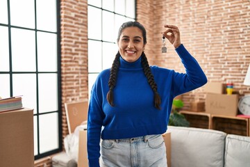 Young hispanic woman smiling confident holding key of new house at new home