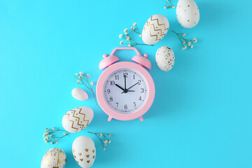 Happy easter concept. Flat lay photo of white gold eggs, gypsophila flowers on pastel blue background and pink alarm clock in the middle. Easter coming idea.