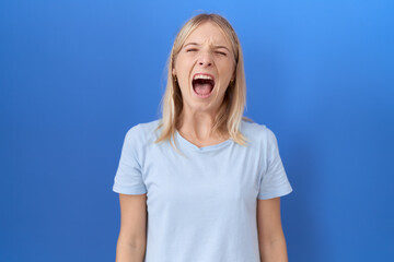 Young caucasian woman wearing casual blue t shirt angry and mad screaming frustrated and furious, shouting with anger. rage and aggressive concept.