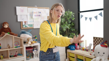 Young blonde woman preschool teacher asking for silence at kindergarten