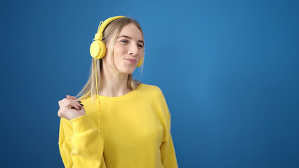 Young blonde woman dancing wearing headphones over isolated blue background