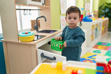 Adorable hispanic boy playing with play kitchen standing at kindergarten