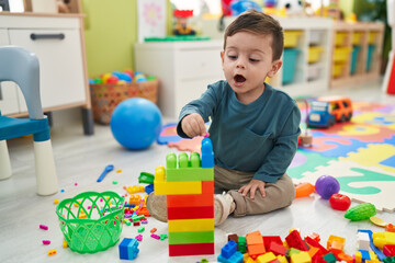 Adorable hispanic boy playing with construction blocks sitting on floor at kindergarten