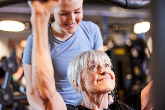 Trainer helping a smiling senior lift weights. Senior woman exercising with personal trainer