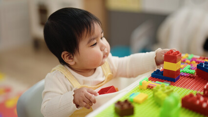 Adorable hispanic baby playing with construction blocks sitting on table at kindergarten