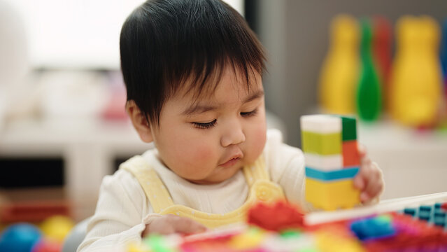 Adorable hispanic baby playing with construction blocks sitting on table at kindergarten