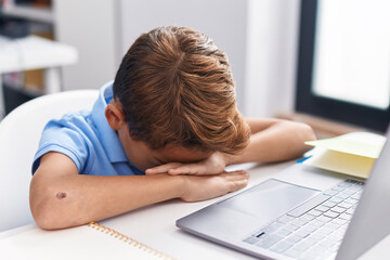 Adorable hispanic boy student using computer with stressed expression at classroom