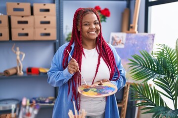 African american woman artist holding paintbrush and palette at art studio
