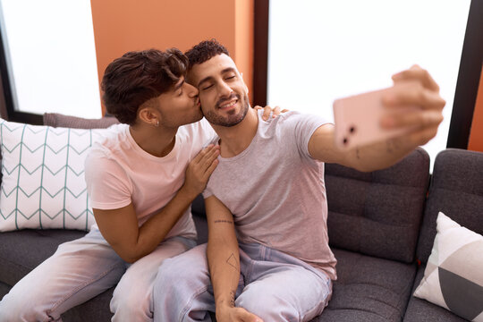 Two hispanic men couple make selfie by smartphone kissing at home
