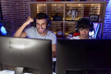 Two hispanic men streamers playing video game with winner expression at gaming room