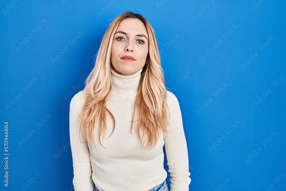 Poster young caucasian woman standing over blue background relaxed with serious expression on face. simple 