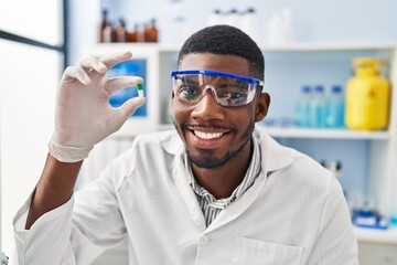 Young african american man wearing scientist uniform holding pill at laboratory