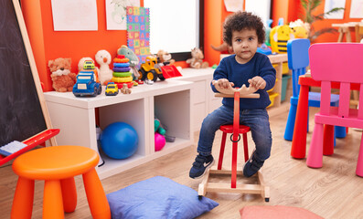 Adorable hispanic toddler playing with reindeer rocking at kindergarten