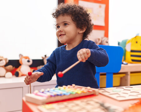 Adorable hispanic toddler playing xylophone standing at kindergarten