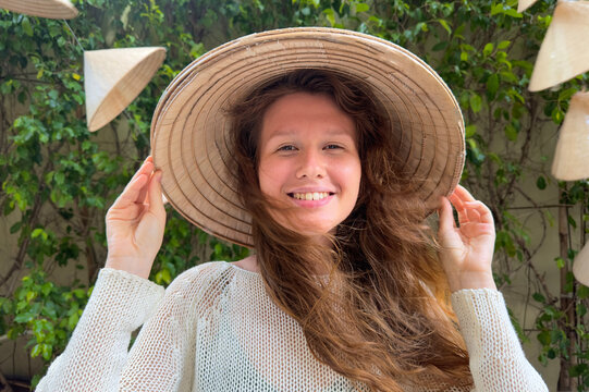 Portrait of happy positive young woman traveler in Vietnamese wicker traditional hat in Asia, Vietnam