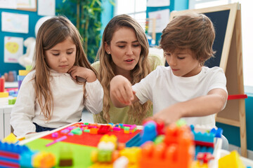 Teacher with boy and girl playing with construction blocks sitting on table at kindergarten