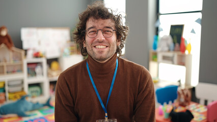 Young hispanic man preschool teacher smiling confident standing at kindergarten