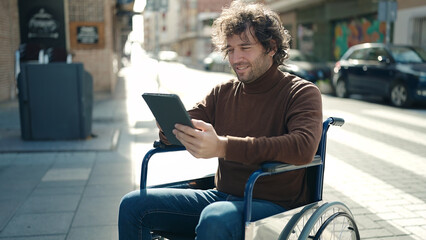 Fototapeta na wymiar Young hispanic man using touchpad sitting on wheelchair at street