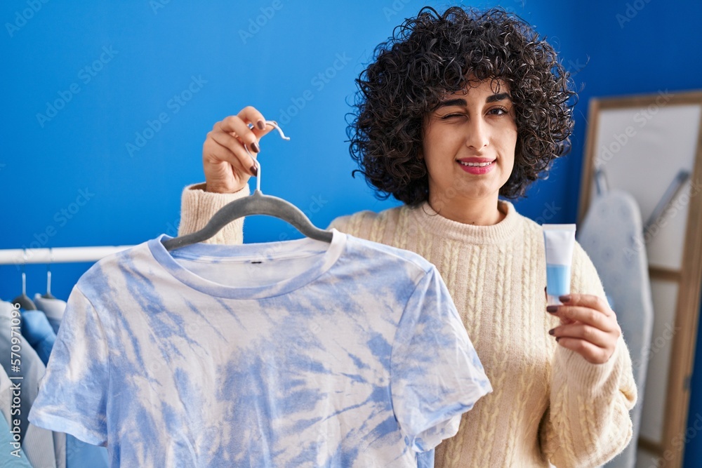 Sticker Young brunette woman with curly hair dyeing tye die t shirt winking looking at the camera with sexy expression, cheerful and happy face.