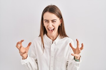 Young caucasian woman standing over isolated background crazy and mad shouting and yelling with...