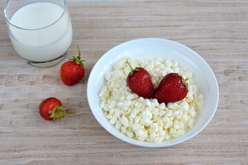 curd cheese in the bowl with stawberry and glass of milk isolated on beige tablecloth, close-up