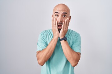 Middle age bald man standing over white background afraid and shocked, surprise and amazed expression with hands on face