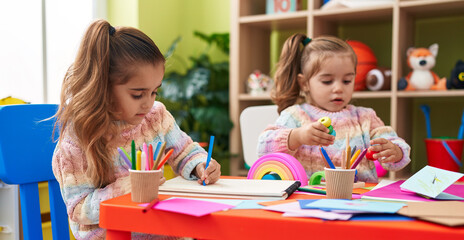 Fototapeta premium Two kids preschool students sitting on table drawing on paper at kindergarten