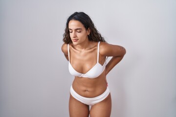 Fototapeta premium Young hispanic woman wearing white lingerie suffering of backache, touching back with hand, muscular pain