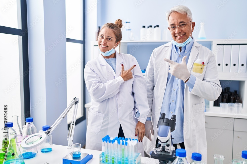 Canvas Prints Middle age hispanic people working at scientist laboratory smiling cheerful pointing with hand and finger up to the side