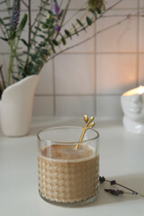 Glass texture cup with coffee latte near vase with bouquet on table in kitchen