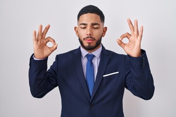 Young hispanic man wearing business suit and tie relaxed and smiling with eyes closed doing meditation gesture with fingers. yoga concept.