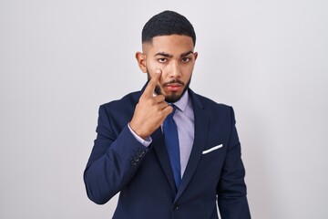 Young hispanic man wearing business suit and tie pointing to the eye watching you gesture, suspicious expression