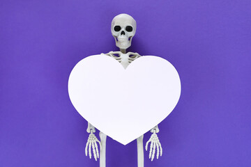 Skeleton with big white blank cut out heart on it, place for text in paper heart frame. Anatomical plastic model human skeleton centered on violet background. Valentine's day love concept.