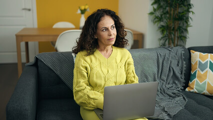 Middle age hispanic woman using laptop sitting on sofa at home