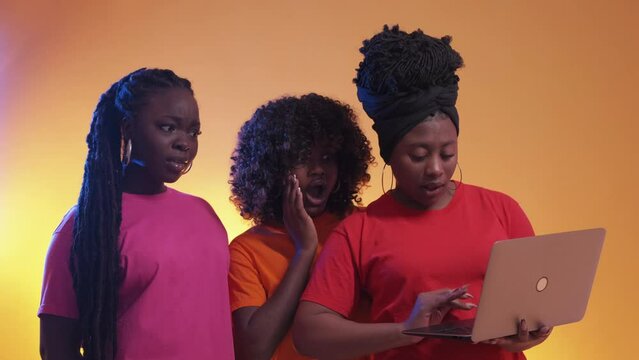 Shocked content. Searching women. Neon light people. Surprised curious black female seeing laptop information posing orange background.