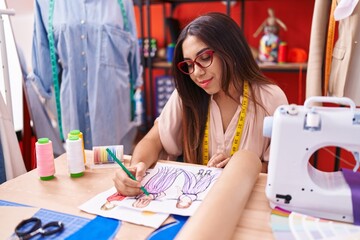 Young beautiful arab woman tailor drawing clothing design on notebook at atelier