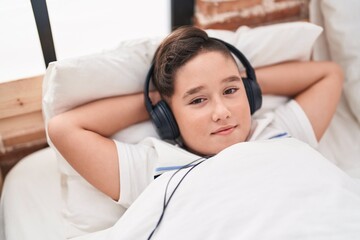 Adorable hispanic boy listening to music lying on bed at bedroom