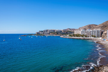 Fototapeta premium Scenic view of beach and ships sailing on beautiful seascape by buildings at coastline. Clear blue sky in the background on a sunny day at Gran Canaria island in Spain