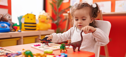Adorable hispanic toddler playing with dino toy sitting on table at kindergarten