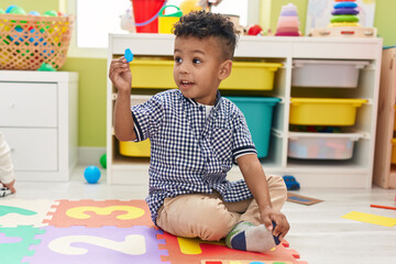 African american boy holding wooden piece sitting on floor at kindergarten