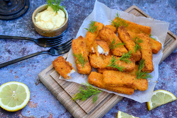 Close up of   Crispy breaded  deep fried fish fingers with breadcrumbs served  with remoulade sauce and  lemon Cod Fish Nuggets on rustic wood table background