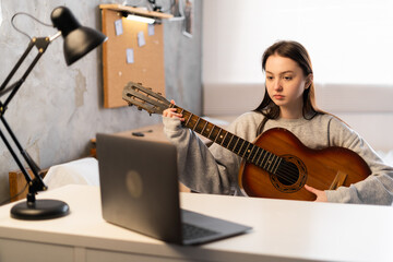 Teenager girl learning to play guitar at home using online lessons. Hobby remote musical education...